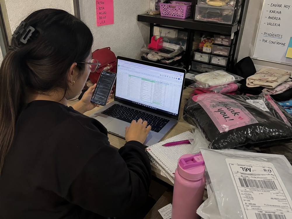 Vendedora registrando pedidos en una hoja de cálculo junto a paquetes listos para enviar