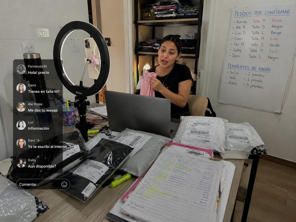 Vendedora en un TikTok Live con comentarios de clientes y pedidos empacados sobre la mesa